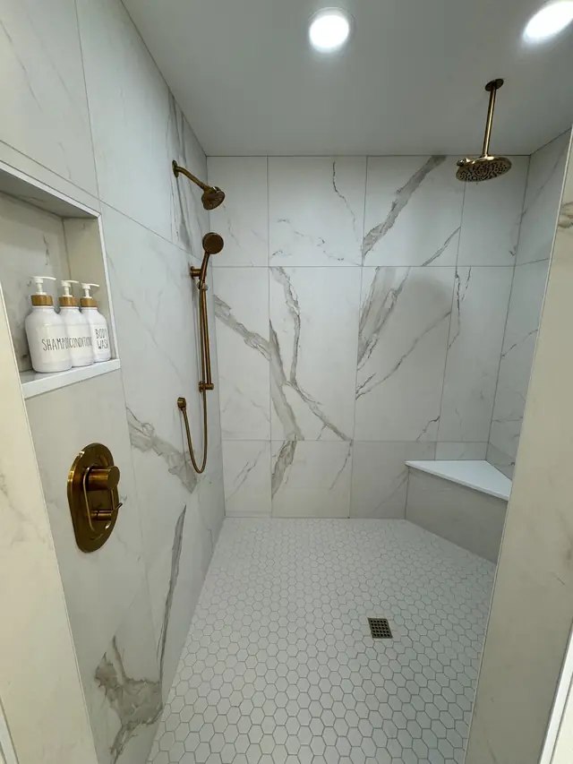 A marble-look walk-in shower with brass fixtures and a niche