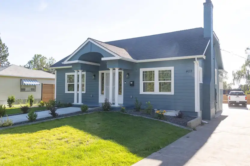 The street-facing front of a finished blue remodeled home with a lawn
