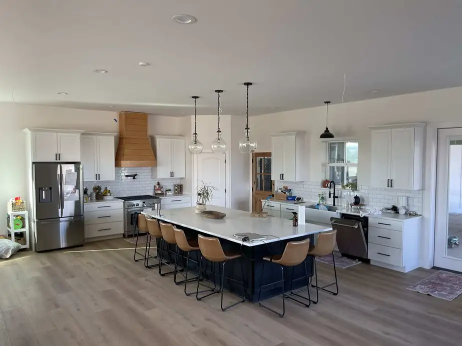 A large white kitchen with a long island, pendant lights and bar stools