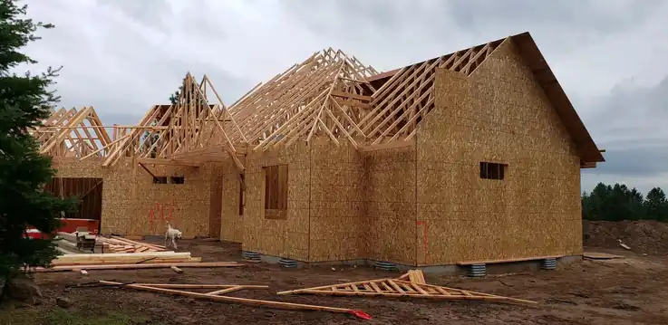 Roof trusses set over sheathed walls on a framed Fisher Construction building, with fresh dirt around the footing