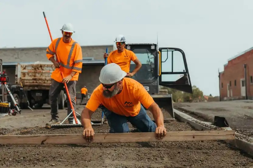 Crew in orange Fisher Construction shirts and hard hats setting forms beside an excavator
